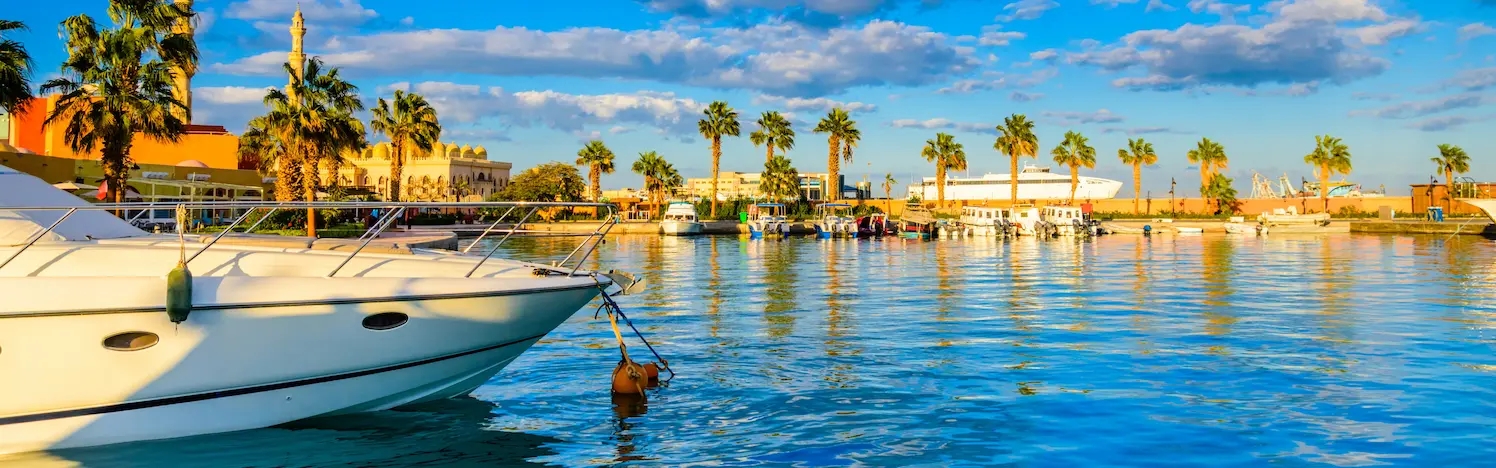 Kleiner Hafen in Hurghada; links im Bild ist der Rumpf einer Yacht, rechts Meer und Palmenpromenade.