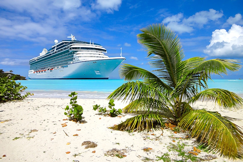 Kreuzfahrtschiff vor einer tropischen Insel mit Palmen, weißem Sandstrand und türkisblauem Meer
