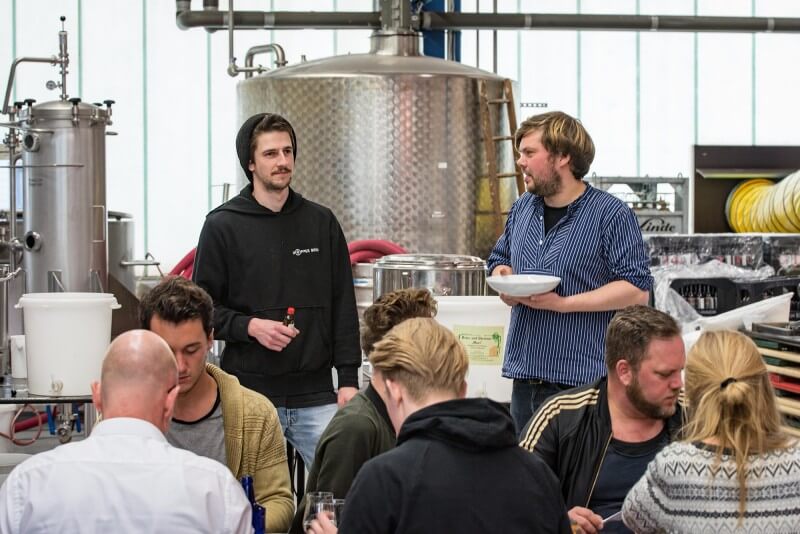 Männer und Frauen essen und trinken neben den Braukesseln