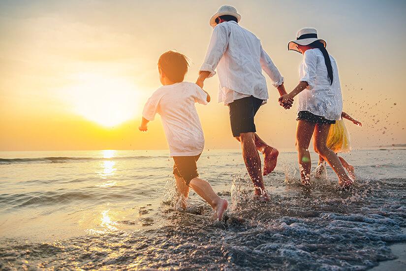 Familie, Hand in Hand mit zwei Kindern spielt am Strand im Wasser Packliste Ferienwohnung Ferienhaus Strand