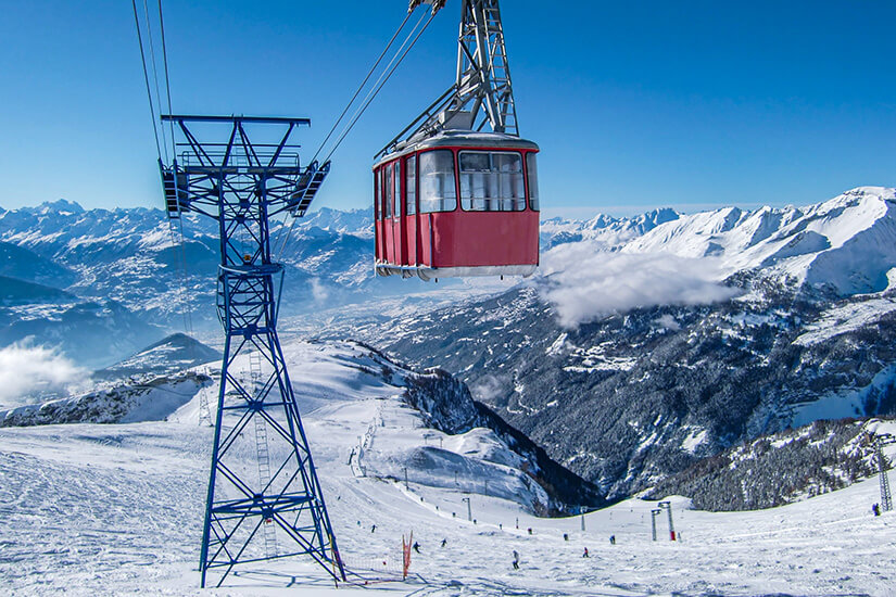 Eine Seilbahn mit roter Gondel schwebt über einer verschneiten Piste in den Schweizer Alpen. Sion Schweiz Ski