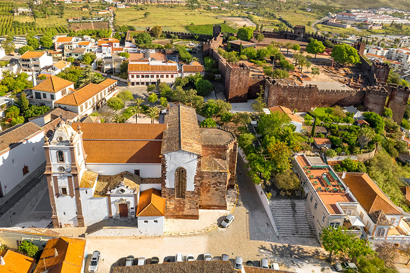 Blick von oben auf die weiße Kathedrale, im Hintergrund ist die Festung zu sehen. Silves Kathedrale