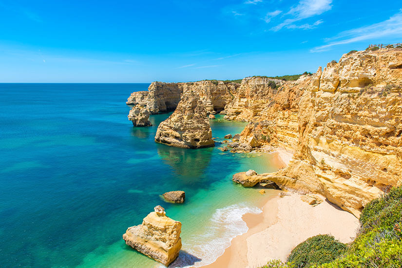 Goldgelber Strand umrahmt von Felsformationen, davor türkisblaues Wasser. Algarve Praia da Marinha