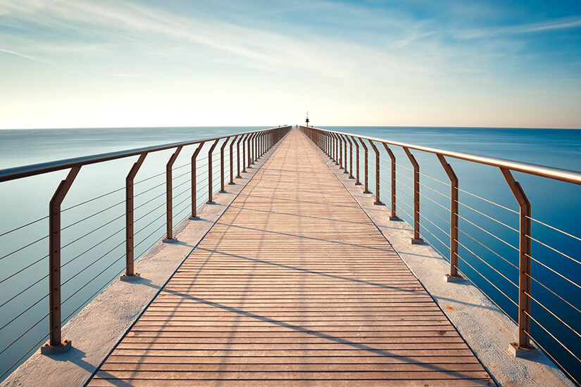 Lange Brücke mit Holzboden und Relings aus Stahl, die in das Meer hinausragt. Badalona Bruecke