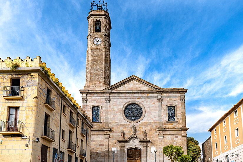 Kirche aus hellem Stein mit einem Glockenturm auf der linken Seite und Rosettenfenster über dem Eingang. Badalona Kirche