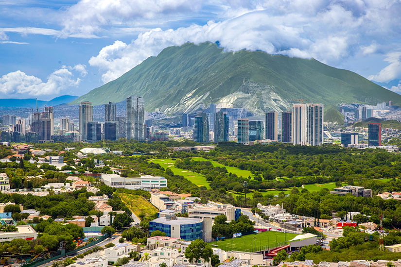 Ein Blick auf die Stadt Monterrey mit ihrer Skyline über den Grünanlagen. Im Hintergrund erhebt sich der majestätische Berg Cerro de la Silla. Monterrey Mexiko Willkommen