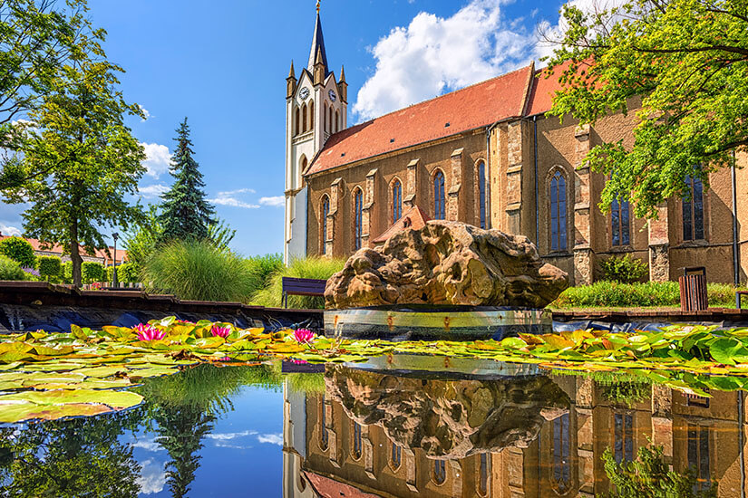 Teich vor einer roten Kirche, auf dem blühende Seerosen zu sehen sind. Keszthely Fruehling