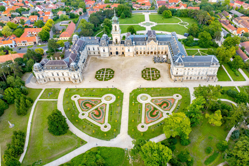 Blick von oben auf ein barockes Schloss umgeben von einer symmetrisch angelegten Parkanlage. Keszthely Schloss