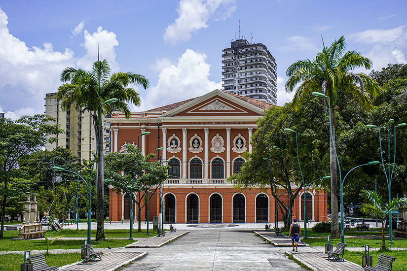 Theater mit weißer Säulenfassade, davor ist ein Park mit Palmen zu sehen. Belem Theater