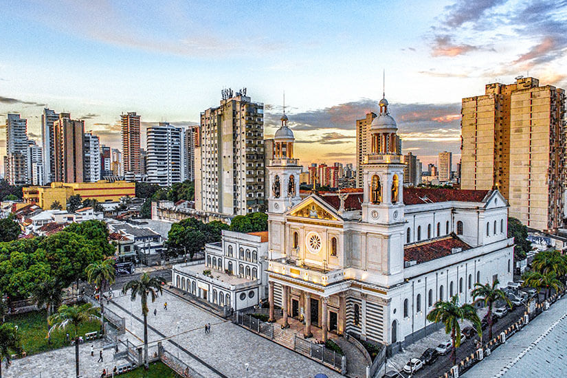 Weiße Kathedrale mit zwei Glockentürmen, davor sind Palmen, im Hintergrund Hochhäuser zu sehen. Belem Kathedrale