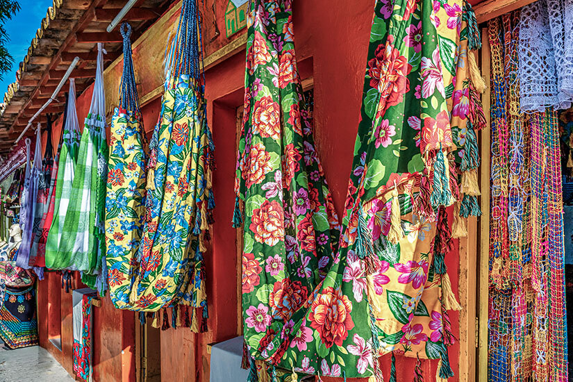 Mehrere farbenfrohe Hängematten mit floralen Mustern hängen dicht nebeneinander an einer Außenwand. Souvenirs Brasilien Haengematten