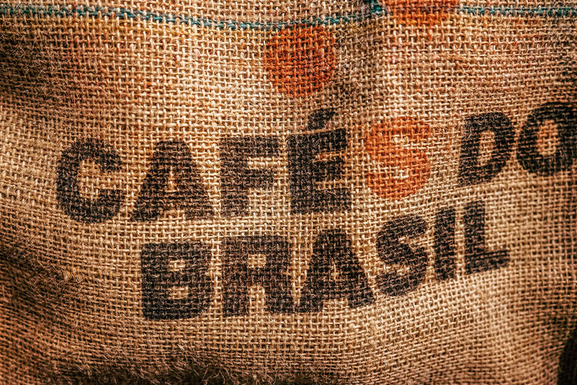 Auf grobem Jutesack-Gewebe steht deutlich die Aufschrift „Cafés do Brasil“. Leichte Falten und der Aufdruck in Schwarz und Orange verleihen dem Material eine gebrauchte, authentische Wirkung. Kaffee Jutesack Brasilien