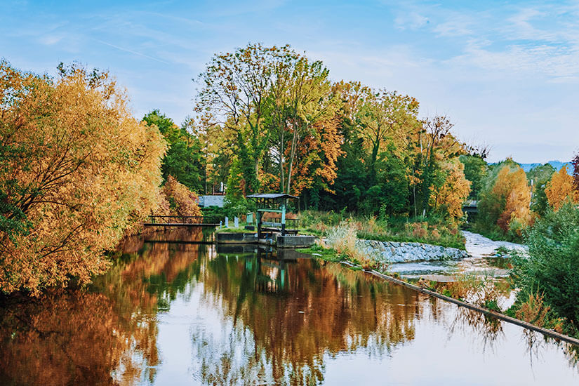 Fluss gesäumt von Bäumen mit bunt verfärbten Laub. Wolfsberg Herbst