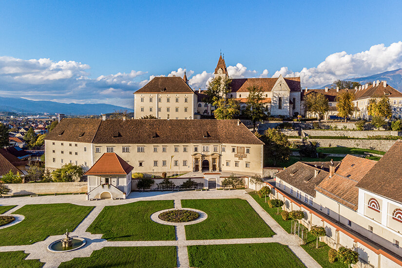 Eine Klosteranlage auf einer Anhöhe, im Vordergrund ist ein barock angelegter Garten zu sehen. Kaernten Stift