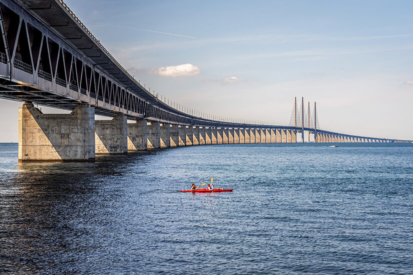 Ein rotes Kajak fährt über die Meerenge Öresund auf die markante Brücke zu. Helsingor Daenemark Kajak