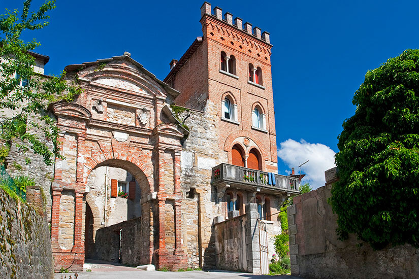 Historisches Stadttor mit Turm und Rundbogen. Davor sind grüne Bäume zu sehen, der Himmel ist blau. Belluno Porta Ruga