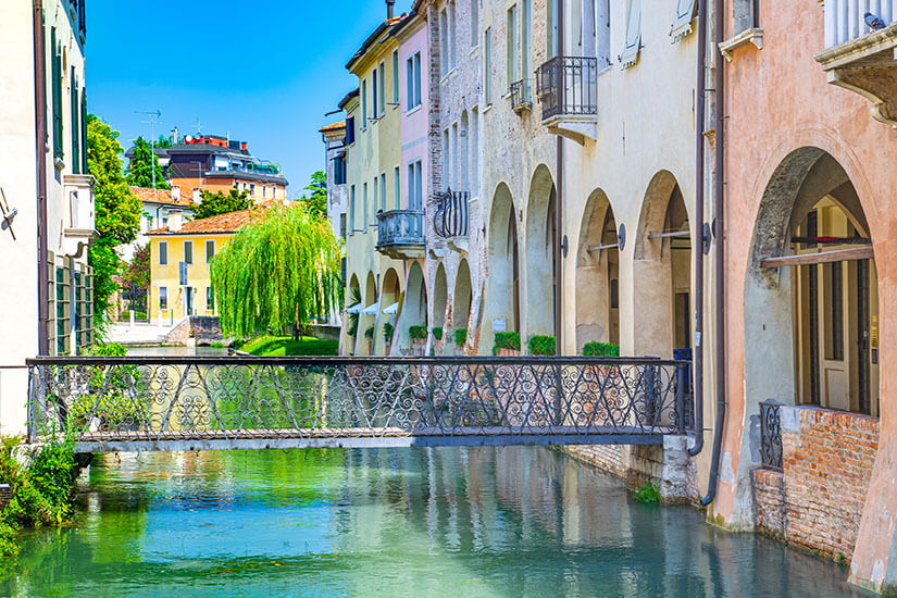 Ein Kanal fließt an einer Häuserzeile vorbei, eine Brücke führt über den Fluss. Italien Treviso