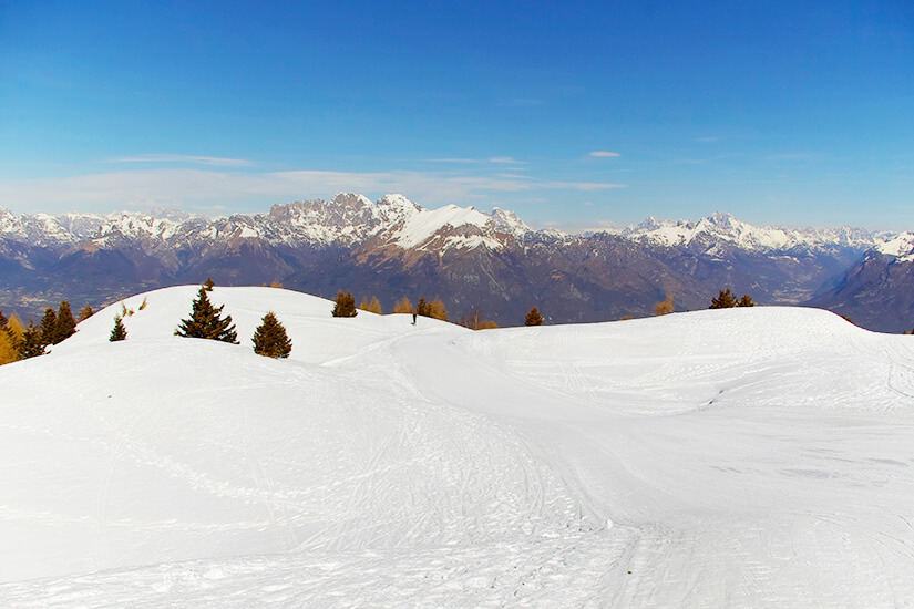 Verschneites Skigebiet unter blauem Himmel. Im Hintergrund ist eine Bergkette zu sehen. Belluno Skigebiet