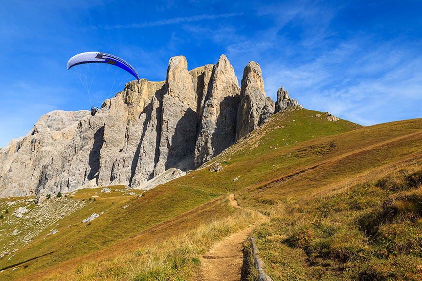 Ein Gleitschirmflieger vor schroffen Felswänden der Dolomiten. Der Himmel ist strahlend blau. Dolomiten Paragliding