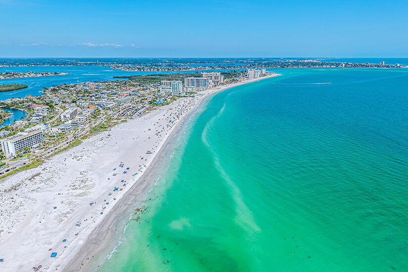 Der Siesta Key Beach in Sarasota an der Westküste Floridas. Türkisblaues klares Wasser trifft auf hellen Sandstrand, im Hintergrund sind Gebäude der Stadt zu sehen. Sarasota USA Strand