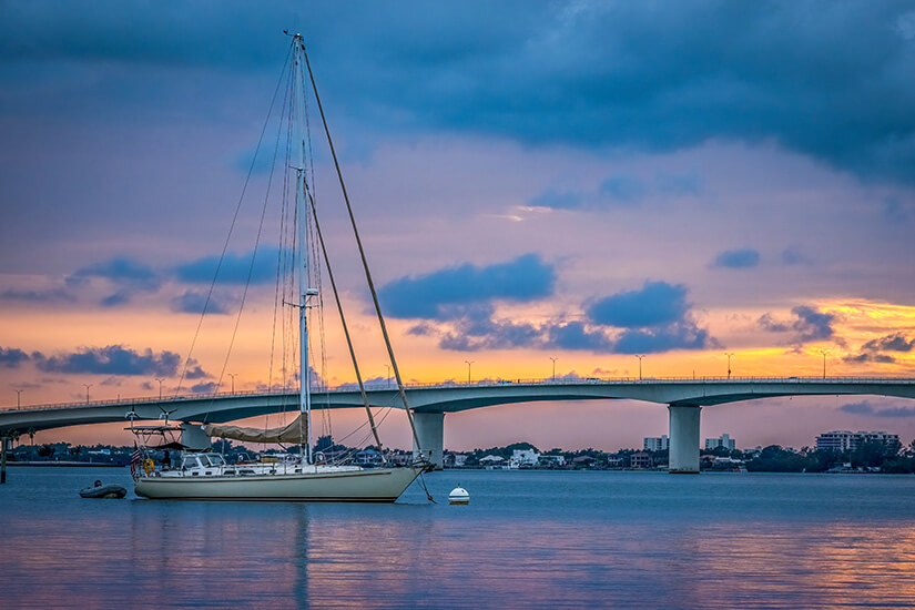 Ein Segelboot gleitet über das Meer. Im Hintergrund ist eine Brücke mit Sonnenuntergang zu sehen. Sarasota USA Sunset