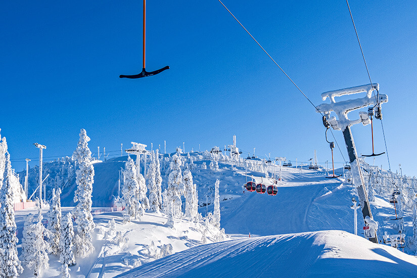 Ein sonniges Skigebiet mit tief verschneiten Pisten, Sesselliften und völlig mit Schnee und Eis überzogenen Bäumen unter strahlend blauem Himmel. Ruka Skigebiet Finnland