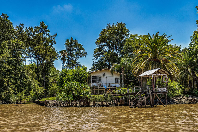 Eine Hütte auf Stelzen über dem Fluss Panará ist zu sehen, umgeben von viel tropischem Grün. Rosario Argentinien Delta