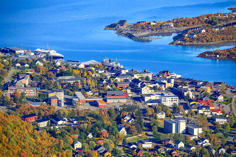 Ein Städtchen auf einer Insel der Vesteralen in Norwegen ist zu sehen. Herbstliche Bäume umgeben den Ort. Im Hintergrund leuchtet ein blauer Fjord. Vesteralen Norwegen Willkommen