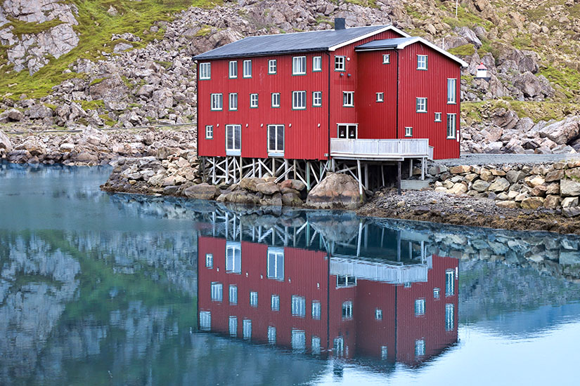 Ein traditionelles Holzhaus in leuchtend roter Farbe spiegelt sich im Wasser wider. Vesteralen Norwegen Fischerdorf
