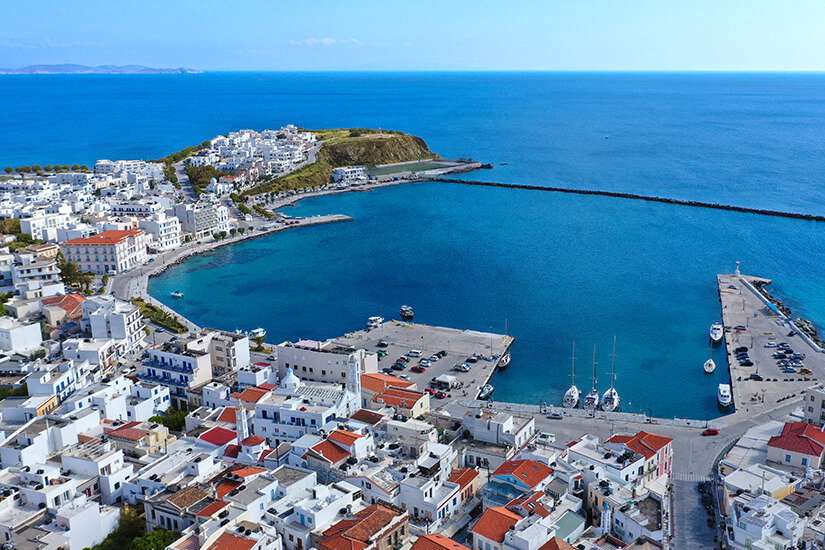 Vogelperspektive vom Hafen in Tinos Stadt. Es sind viele Gebäude in typischer Kykladen-Architektur und das Meer sichtar. Tinos Griechenland Hafen