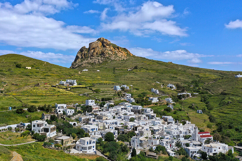 Weiße Häuser an einem Hang. Dahinter ist der markante Felsen des Exomvourgo sichtbar. Tinos Griechenland Tripotamos