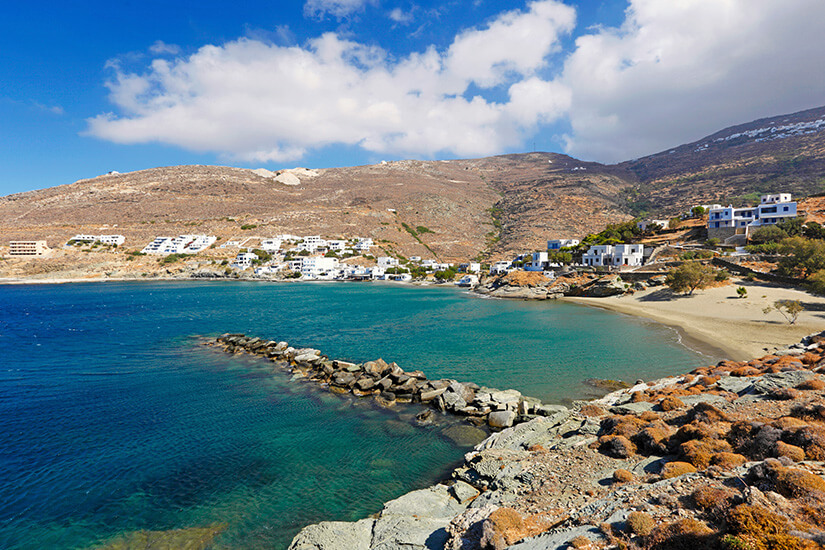 Das Dorf Isternia liegt direkt am Meer. Im Hintergrund erstreckt sich die Hügellandschaft und im Vordergrund ist ein Strand mit Felsen. Tinos Griechenland Strand