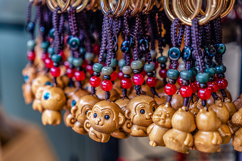 Mehrere Schlüsselanhänger hängen dicht nebeneinander an einem Ring und zeigen kleine, geschnitzte Figuren. Zwischen den Anhängern sind rote und grüne Perlen sowie geflochtene Schnüre zu sehen. Schluesselanhaenger Suedkorea