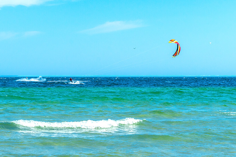 Kitesurfer auf dem offenen Wasser mit buntem Kite. Das Meer schimmert in verschiedenen Blau- und Grüntönen und hat Wellen. Polen Ostsee Kitesurfer