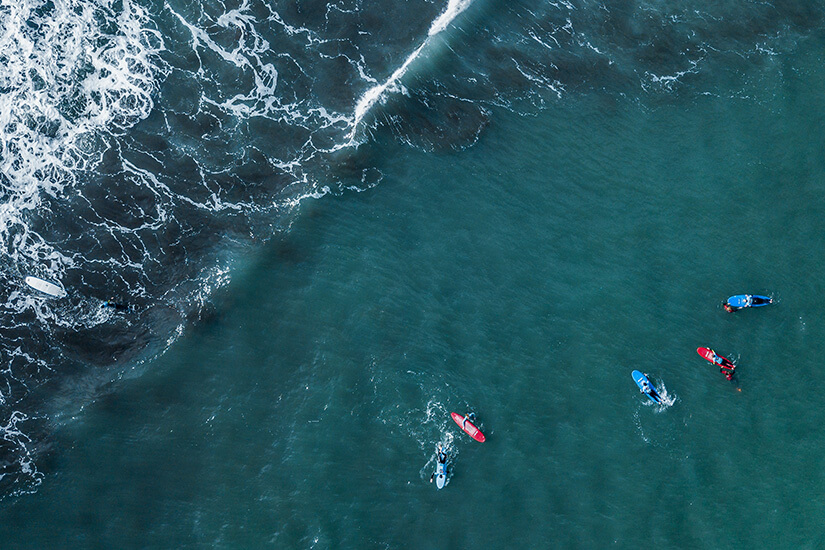Surfer auf dem Board direkt vor einer hohen, brechenden Atlantikwelle. Die Wasseroberfläche ist tiefblau, mit weißer Gischt an der Wellenkante. Machico Portugal Surfer