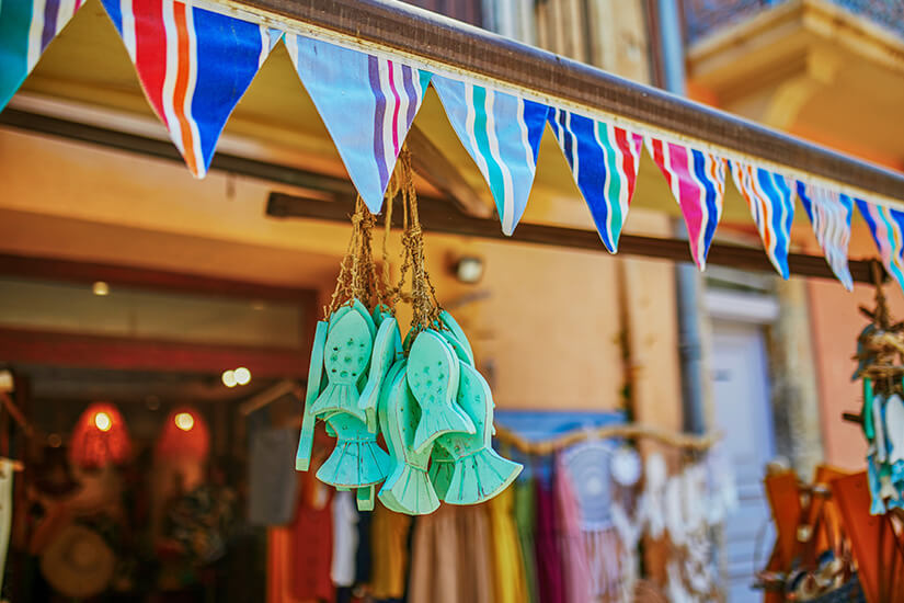 Blick vom blauen Meer auf die bunte Hafenpromenade von Port-Vendres mit Fischerbooten, einem roten Rettungsschiff und einer Häuserzeile in mediterranen Farben unter strahlendem Himmel. Collioure Frankreich Souvenirs