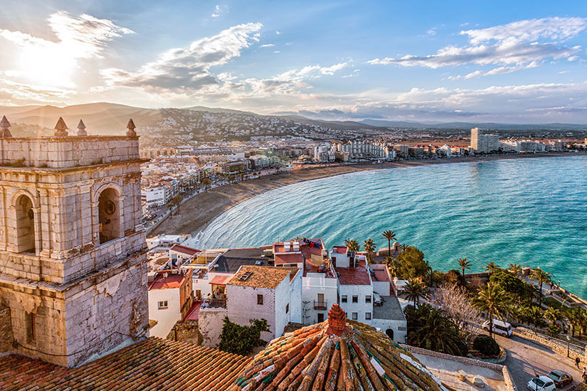 Die mittelalterliche Festungsstadt Peñíscola thront majestätisch über dem türkisblauen Mittelmeer, während die goldene Abendsonne die alte Steinkirche in warmes Licht taucht. Der geschwungene Sandstrand erstreckt sich bis zum modernen Stadtteil am Horizont. Ein Ort, an dem sich Geschichte und Mittelmeer-Idylle auf magische Weise verbinden. Städte Spanien Valencia