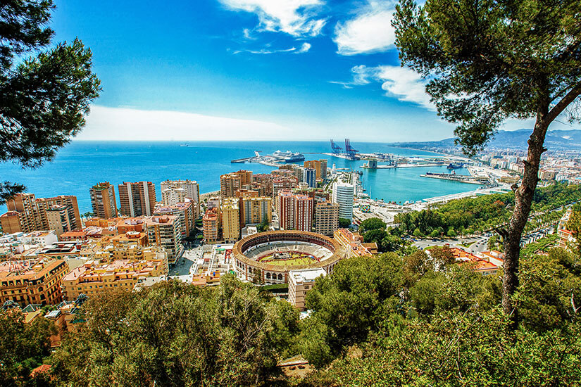 Vom grünen Hügel des Castillo de Gibralfaro aus bietet sich ein atemberaubender Blick über Málaga: Hochhäuser, der runde Stierkampfring, der geschäftige Hafen und das endlose Blau des Mittelmeers verschmelzen zu einem faszinierenden Panorama. Pinien rahmen die Szenerie wie ein natürlicher Bilderrahmen. Städte Spanien Málaga