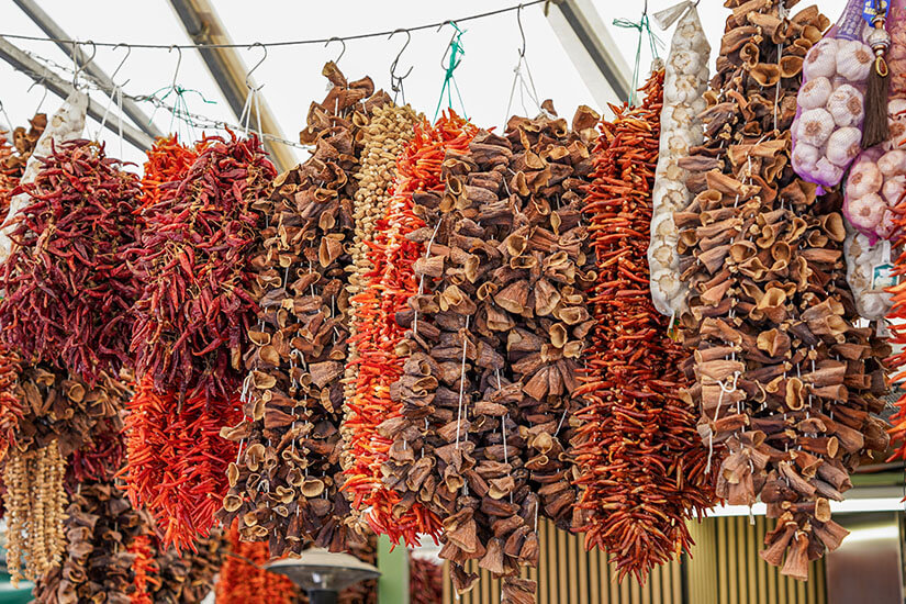 Dichte Bündel aus getrockneten Chilischoten, Knoblauch und anderen Gewürzen hängen an Haken nebeneinander. Souvenirs Chile Chili