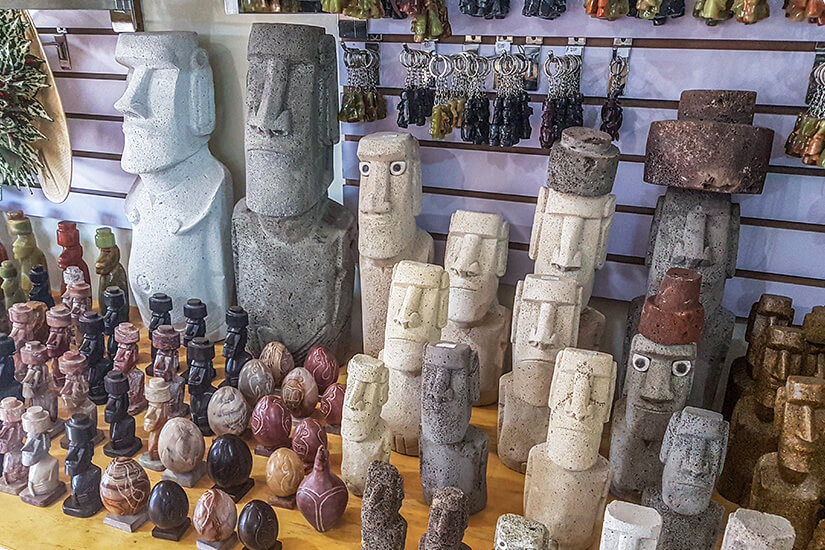 Mehrere steinerne Figuren mit länglichen Gesichtern stehen dicht nebeneinander auf einem Tisch. Moai Osterinseln