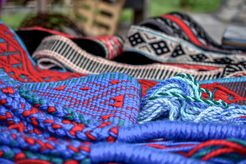 Mehrere gewebte Textilien mit kräftigen Blau-, Rot- und Schwarztönen liegen übereinander ausgebreitet. Souvenirs Chile Mapuche