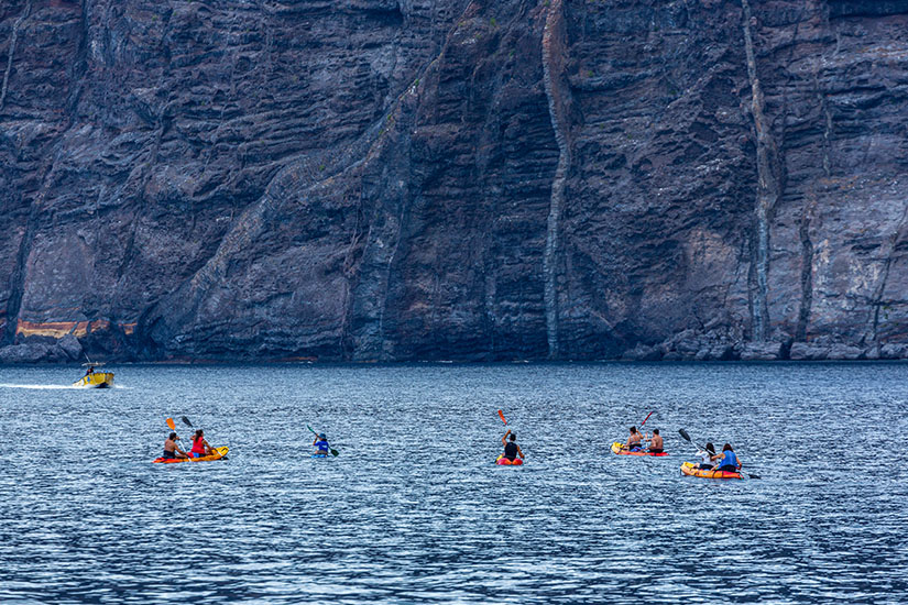 Mehrere gelbe und rote Kajaks und Kanus gleiten über das Meer bei den Klippen Los Gigantes. Puerto de Santiago Spanien Kajak