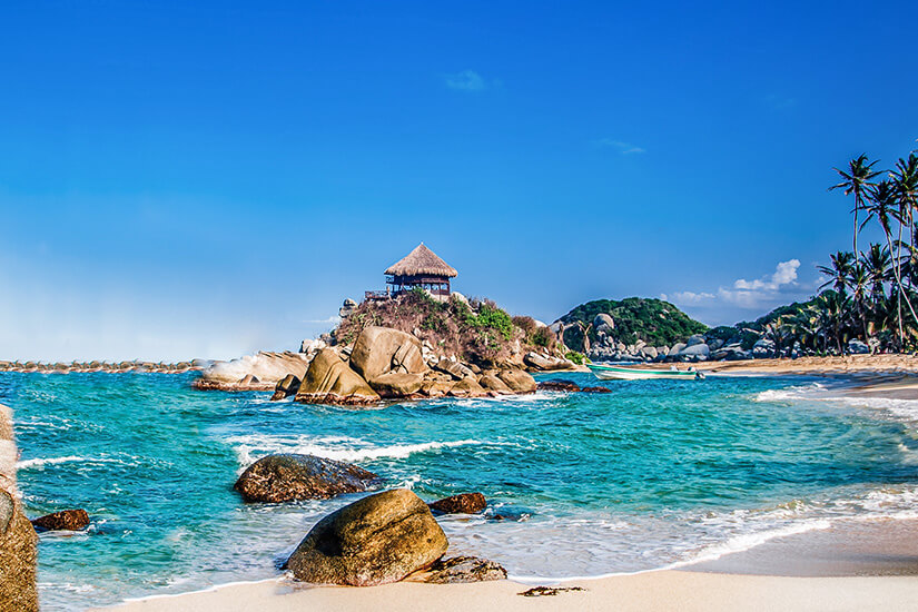 Türkisfarbenes Meer und große Felsen am Strand von Cabo San Juan mit der berühmten Holzhütte auf einem Hügel. Tayrona Nationalpark Cabo San Juan