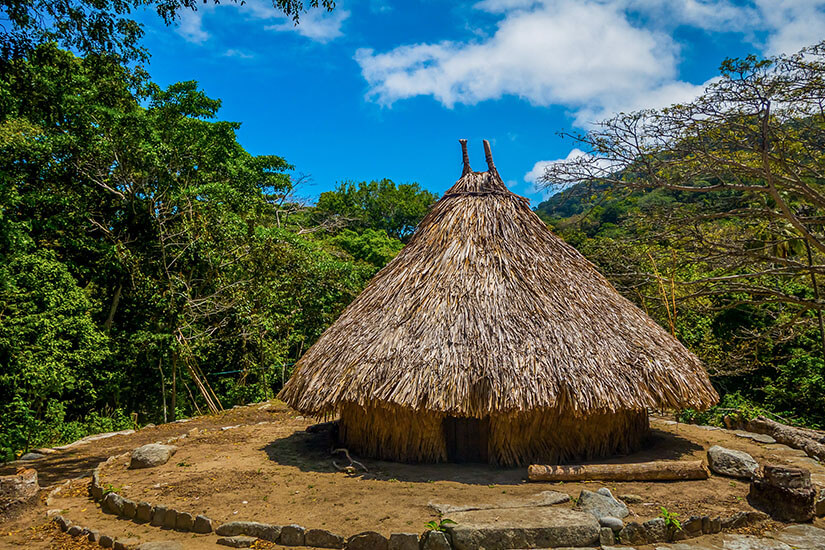 Ein traditionelles rundes indigenes Haus mit kegelförmigem Strohdach auf einer Steinterrasse inmitten von grünem Dschungel. Tayrona Nationalpark Pueblito Chairama