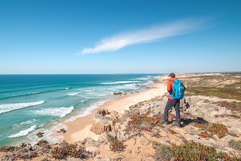 Türkisfarbenes Meer und sanfte Wellen erstrecken sich bis zum Horizont unter klarem Himmel. Die Szene vermittelt Weite, Freiheit und Abenteuerlust. Packliste Portugal Strand