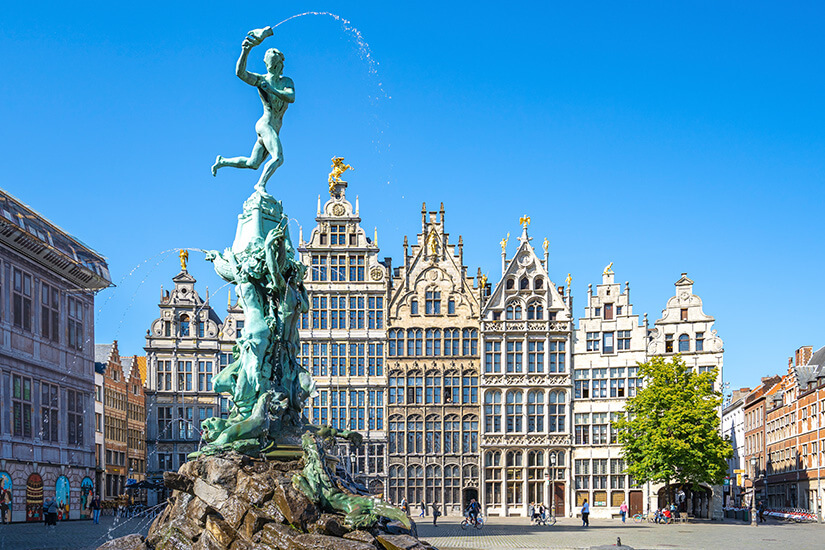 Wasserfontänen spritzen aus dem Brunnen und im Hintergrund säumen prachtvolle Gildehäuser mit goldverzierten Giebeln und kunstvollen Fassaden den Platz. Staedte Belgien Antwerpen