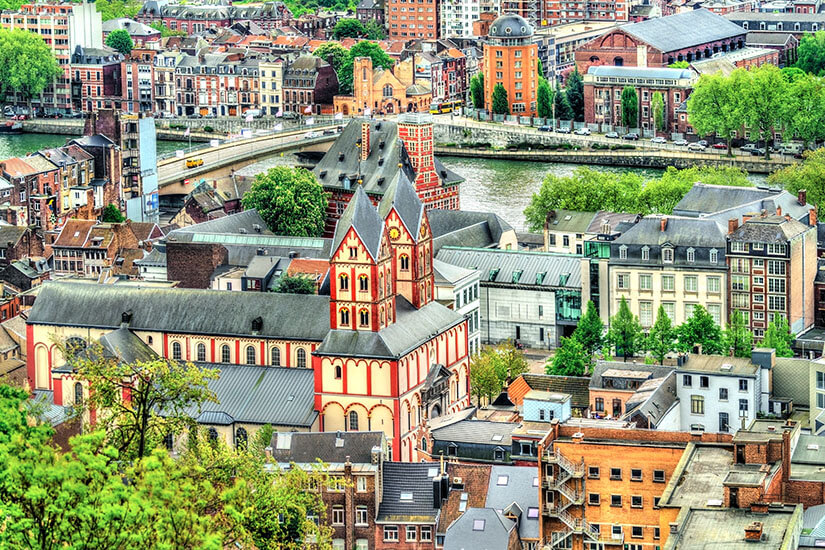 Eine markante rot-weiß gestreifte Stiftskirche mit romanischem Westwerk dominiert dieses Stadtpanorama, während sich dahinter die Maas mit ihren Brücken durch ein Häusermeer zieht. Staedte Belgien Luettich
