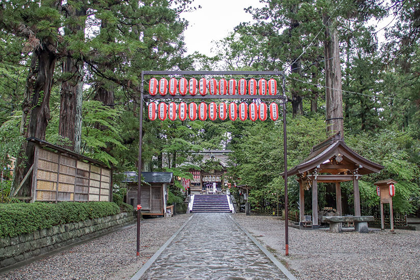 Ein traditioneller Schreineingang, gesäumt von mächtigen Zedern und geschmückt mit roten Laternen. Die steinerne Treppe führt tiefer in das schattige Heiligtum – ein Ort der Stille fernab des Großstadttrubels. Städte Japan Sendai