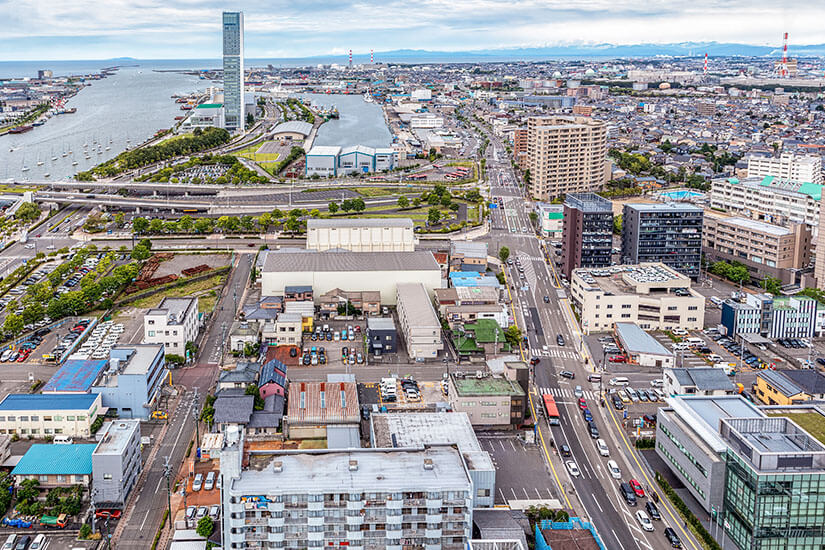 Luftaufnahme der Hafenstadt Niigata mit Blick auf den Shinano-Fluss und das Japanische Meer. Die Mischung aus Wohnvierteln, Hafenanlagen und dem weiten Horizont zeigt den maritimen Charakter dieses Geheimtipps. Städte Japan Niigata