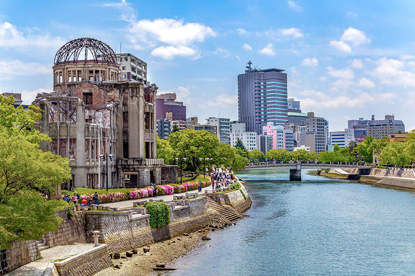 Die Atombomben-Kuppel am Ufer des Flusses Motoyasu, umgeben von saftigem Grün und der modernen Skyline Hiroshimas. Das UNESCO-Weltkulturerbe gehört zu den bewegendsten Gedenkstätten des Landes. Städte Japan Hiroshima